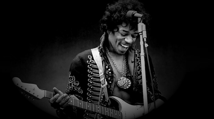 B&W photo of Jimi playing guitar, smiling, relaxed.