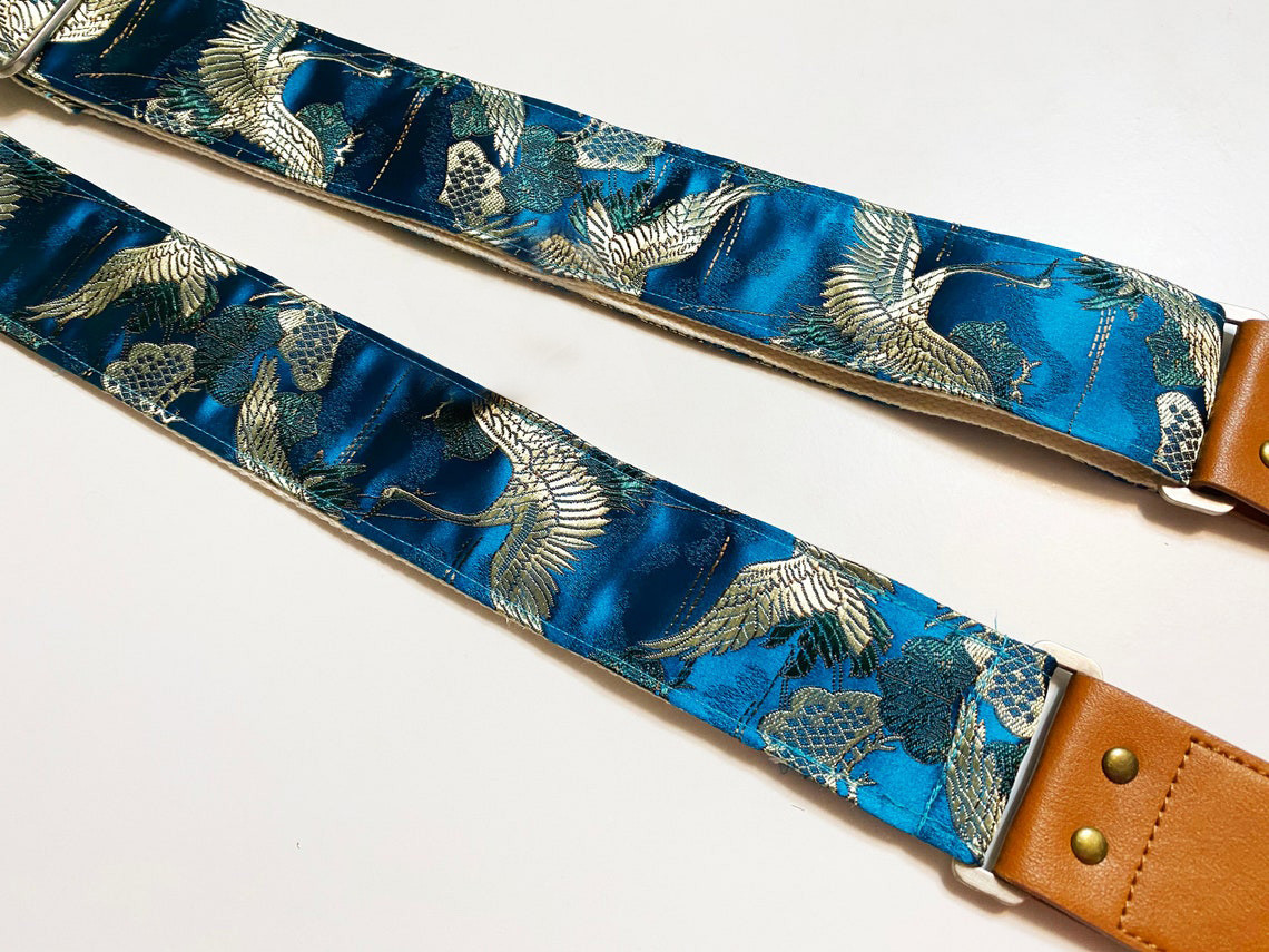 A beautiful blue satin guitar strap, with silver/gold cranes flying in a Japanese/Chinese style. 

