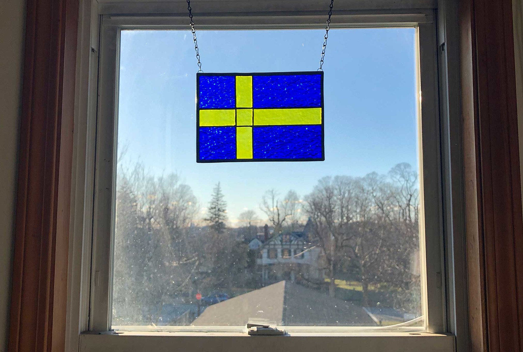 A small flag of Sweden (a yellow cross on a dark blue background) 

hanging in my bedroom window, with the sun shining through.