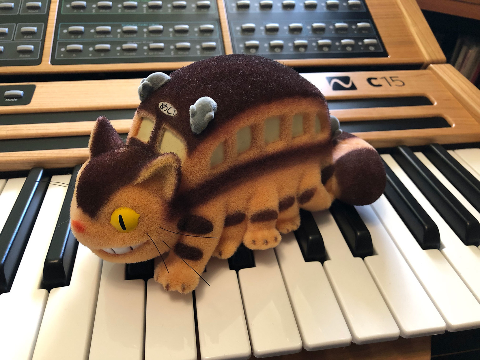 A very well-made toy version of the Catbus from Miyazaki’s film ‘My Neighbor Totoro,’ 

sitting on the keyboard of the Nonlinear Labs C15 synth.