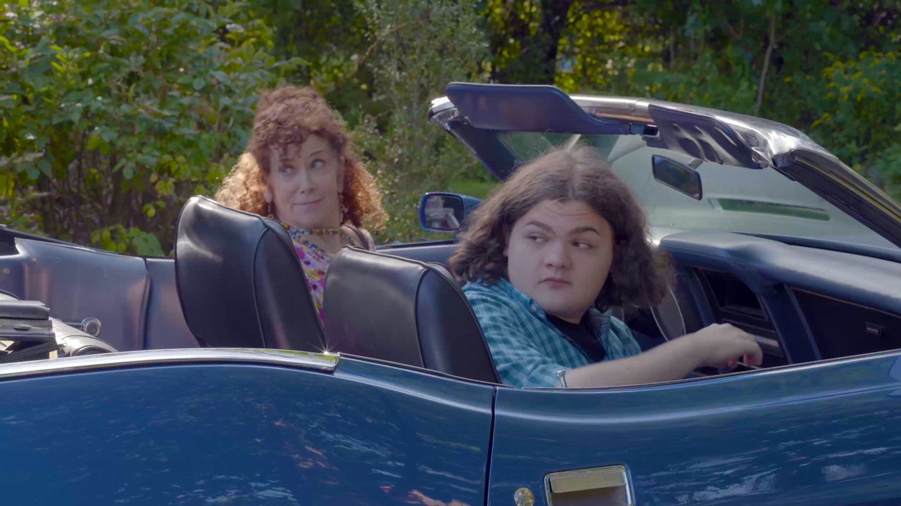 Amy Stiller and Alexander Jameson sitting in a blue convertible, just about to drive off.