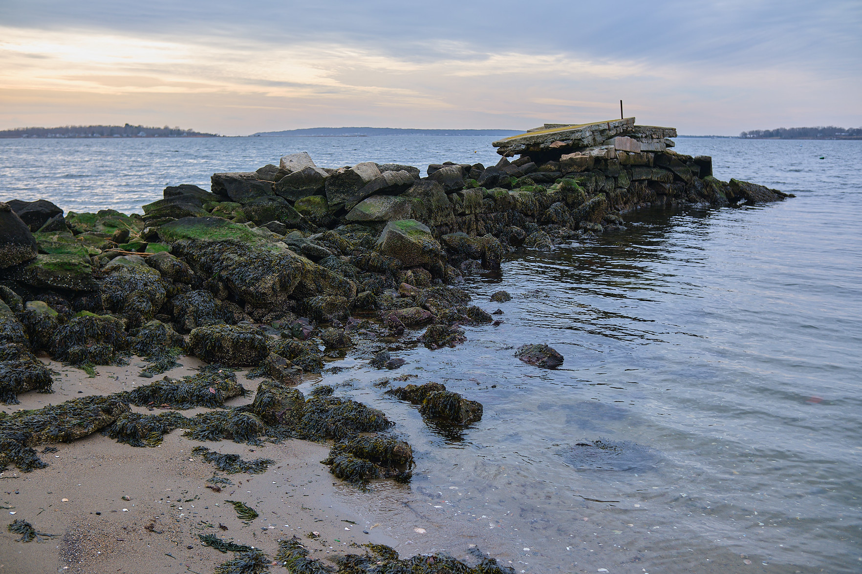 A breakwater extending from a sandy cove.