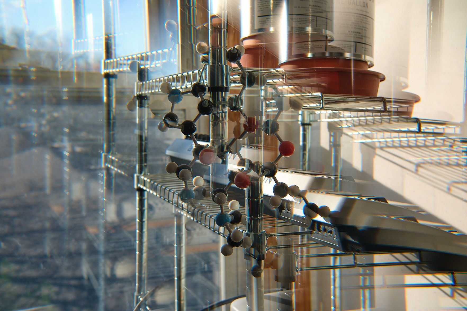 A molecular model on a polished metal stand, reflected in a window and echoed by the filter.